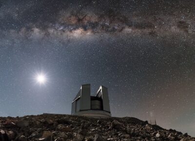 ESO’s astronomical facilities in Chile are hives of activity — or oases! — in the otherwise barren and arid landscape of the Atacama Desert. This hostile and hard-to-reach location may seem like an odd choice for construction, but the Atacama is one of the best sites in the world for astronomy. It has practically no cloud cover, a distinct lack of light pollution, and is the driest non-polar location in the world, receiving under two centimetres of rainfall every year! Chile has hosted ESO’s telescopes since the 1960s, in observatories based at La Silla, Paranal, and Chajnantor Plateau. Shown here is the Visible and Infrared Survey Telescope for Astronomy (VISTA), situated at the Paranal Observatory.  Perched atop a mountain adjacent to Cerro Paranal, the home of the flagship Very Large Telescope (VLT), VISTA is the largest telescope in the world designed to survey the sky in near-infrared light (just beyond that visible to humans). The spectacular sights of the cosmos — including the notable streak of our home galaxy, the Milky Way, stretching across the top of the frame here — are more than enough to keep VISTA and its telescopic siblings busy.